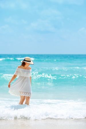 Woman in white dress walking on the beach during summer vacationの写真素材