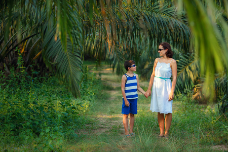 Young woman and her little son walking in tropical forestの写真素材