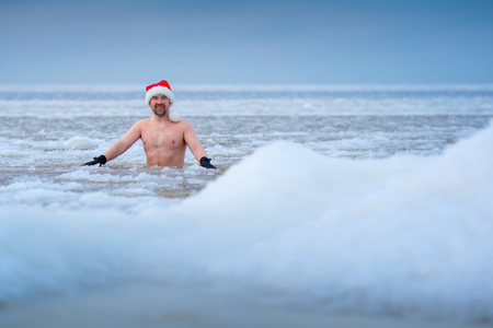 Winter bather in a Santas hat stays in a frozen seaの写真素材