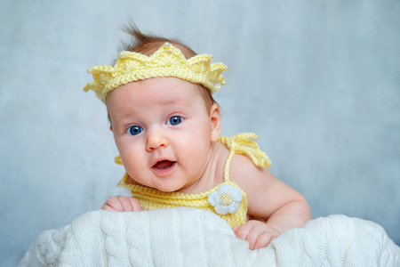 Portrait of a cute newborn baby girl in yellow knitted crown lying on her stomachの写真素材