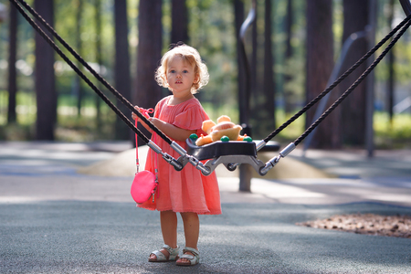Sweet blond little baby girl in beautiful apricot dress plays walks outdoors at playgroundの写真素材