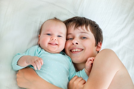 Cute boy and newborn baby girl. Toddler kid hugging his sibling.