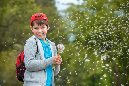Happy child blowing dandelion flower outdoors. Boy having fun in spring park. Blurred green backgroundの写真素材