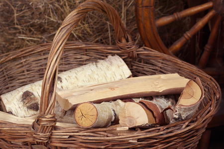 Split birch logs lie in a wicker basket with a handle on the background of haystacks and spindlesの写真素材