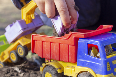 the child is playing on the street with sand; he loads the excavator bucket with earth into the dump truck toyの写真素材