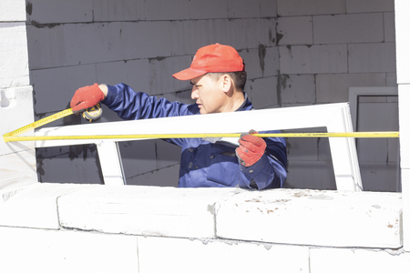workers install glazing in a house under construction, make measurements, drill, saw grinderの写真素材