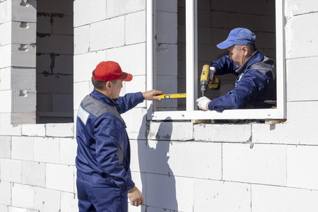 workers install glazing in a house under construction, make measurements, drill, saw grinderの写真素材