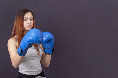 copyspace boxer girl in blue boxing gloves in a gray t-shirt in the rack backgroundの写真素材