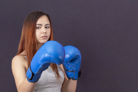 boxer girl in blue boxing gloves in a gray t-shirt in the rack on a gray background copyspaceの写真素材