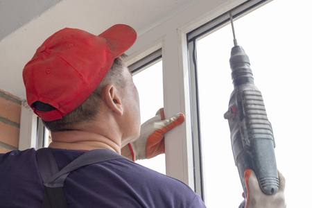 Worker installs windows craftsmen screw the frame to the wall Repair in a high-rise buildingの写真素材