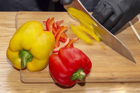 slicing paprika cook. cooking healthy food. diet healthy food. wooden cutting board on wooden table, chef hands in black rubber glovesの写真素材