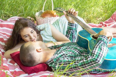 the guy plays the guitar to his girlfriend. romantic meeting. summer picnic couple laying on the grassの写真素材
