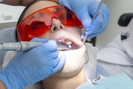 girl on examination at the dentist. treatment of carious tooth. the doctor uses a mirror on the handle and a boron machineの写真素材