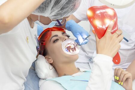 girl patient at the reception at the dentist. treatment of carious tooth. the girl lies on the dental chair with his mouth open. A dentist and his assistant are treating a toothの写真素材
