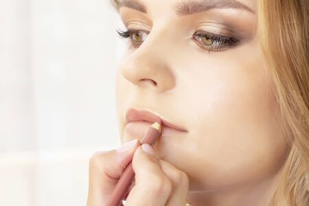 Makeup artist puts make up on girl model. wedding makeup, evening makeup, natural makeup. make-up artist paints lips of girlの写真素材