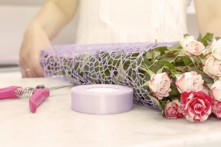 florist girl working in a flower shop. Soft shades of fresh spring flowers, wrapped in decorative paper. Floristry business. Floristry courses. Learn to master the art of ikebana. Florist shares her skills showing how to arrange flowers in a perfect beautiful bouquetの写真素材