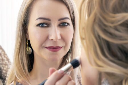 Professional makeup artist working with client in salon. Makeup artist applies highlighter on the face of a girlの写真素材