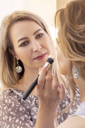 Makeup artist puts make up on girl model. wedding makeup, evening makeup, natural makeup. make-up artist puts eye shadow on eyelids. vertical photoの写真素材