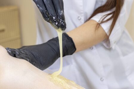Beautician depilating womans legs with liquid sugar in spa center. Depilation Of Legs With Sugar Paste.の写真素材