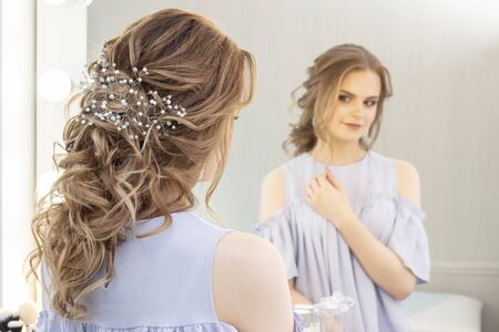 beautiful girl with a wedding hairstyle looks at herself in the mirror, portrait of a young girl. beautiful make-up. beauty saloonの写真素材