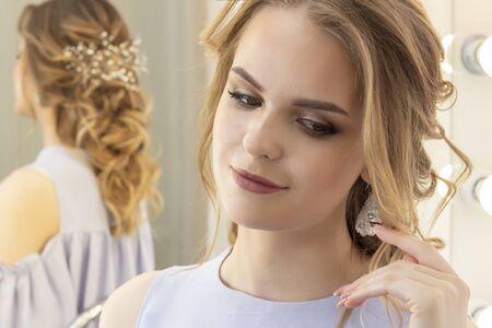 beautiful girl with a wedding hairstyle looks at herself in the mirror, portrait of a young girl. beautiful make-up. beauty saloonの写真素材