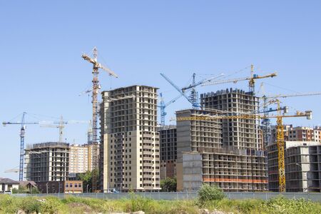 Construction site background. Hoisting cranes and new multi-storey buildings. tower crane and unfinished high-rise building. many cranesの写真素材