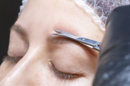 eyebrow shaping in a beauty salon. the girl is trimmed with scissors for extra hair on her eyebrows. master browsの写真素材
