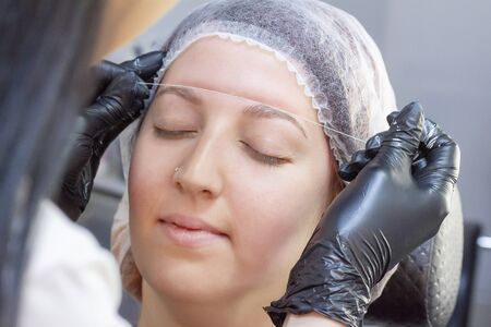 eyebrow dyeing. beauty saloon. the girl lies with her eyes closed on the eyebrow dyeing procedure. preparation of eyebrows for painting. applying cream around the eyebrows using thread.の写真素材