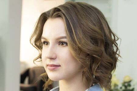 Girl with curled hair sitting in a chair in a beauty studio.の写真素材