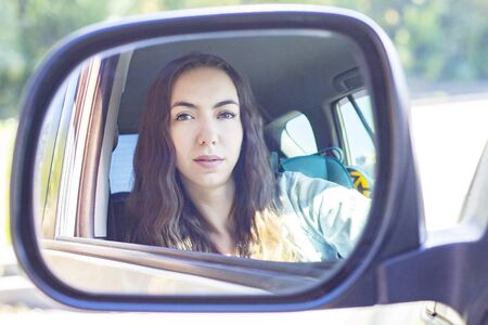 Young woman driving her car. Attractive young girl driver in new car. driver girl looks in the side view mirrorの写真素材