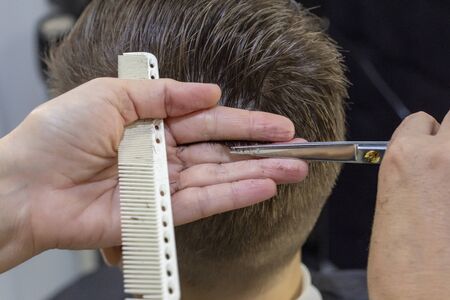 The hands of young barber making haircut to attractive man in barbershop. mens hair cutting scissors in a beauty salonの写真素材