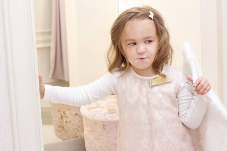 shopping. discounts. little girl shopaholic. girl trying on a beautiful dress gently pink in the fitting room of the boutique. shopping center, shopping. emotionsの写真素材
