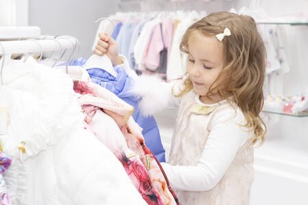 shopping. discounts. little girl shopaholic. girl delighted with beautiful jackets, chooses warm clothes. shopping center, shopping. emotionsの写真素材