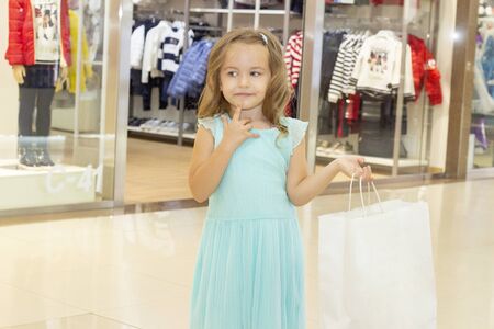 shopping. discounts. little girl shopaholic. girl with shopping bags in hands. white bags copyspace. shopping center, shopping. emotionsの写真素材