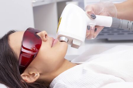 procedure of photoepilation in the beauty salon. Young Woman Receiving Epilation Laser Treatment On Face At Beauty Center Close Upの写真素材