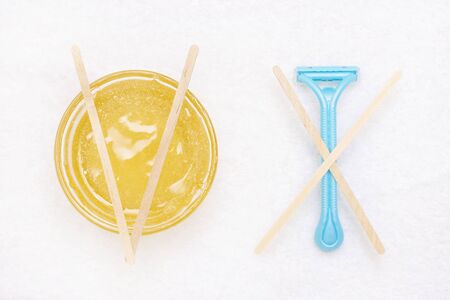 Flat lay top view of a can of wax, paste for shugaring against a razor to remove hair on a white background. Depilation concept.
on the razor are sticks in the form of a cross, on sugar paste the sticks are in the form of a tickの写真素材