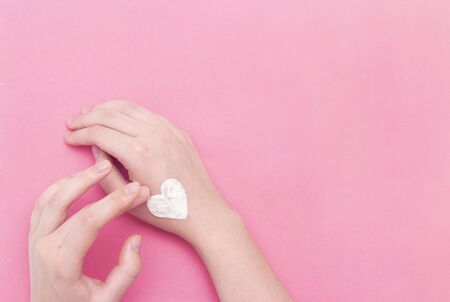 Hands of a beautiful well-groomed woman with a cream jar on a pink textural background. Moisturizer...