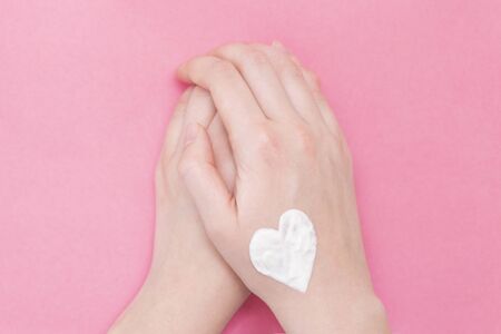 Hands of a beautiful well-groomed woman on a pink textural background. Moisturizer for clean and soft skin in winter. Heart shape made of cream. I love the body. Healthcare concept.の写真素材