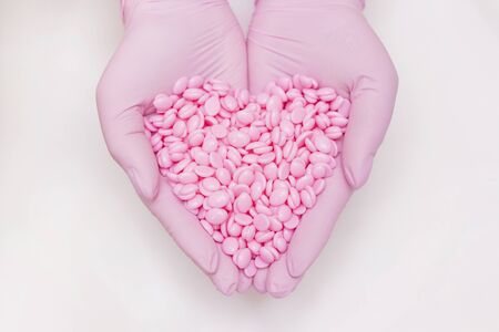 Wax for depilation of pink color. in hands in pink gloves in the shape of a heart. On white background. The concept of waxing, smooth skin.の写真素材