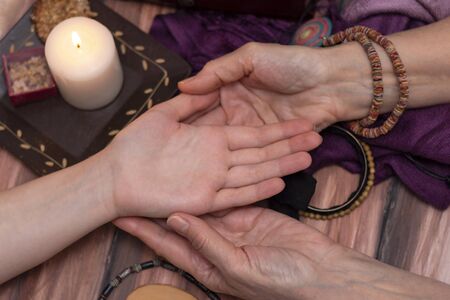 Witch fortune teller reading fortune on girls hand. The concept of magic, predictions of the future, Christmas time. Dark background by candlelightの写真素材
