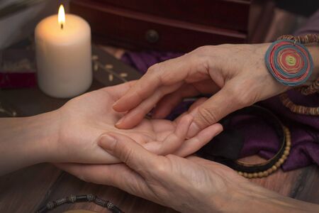 Witch fortune teller reading fortune on girls hand. The concept of magic, predictions of the future, Christmas time. Dark background by candlelightの写真素材