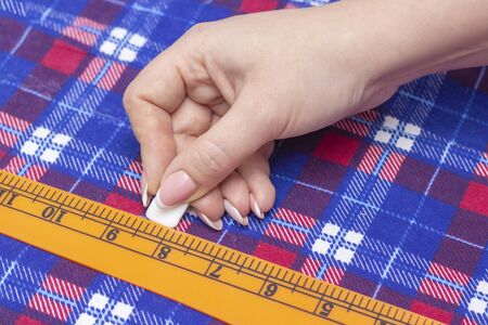 tailor measures the fabric for sewing a shirt. checkered material lies on the table, the tailor draws a strip with a special chalk for fabric using a ruler.の写真素材