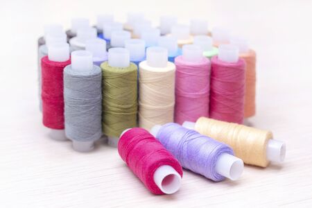 threads on spools of different colors lie on a light wooden table. Three spools of thread are lying....