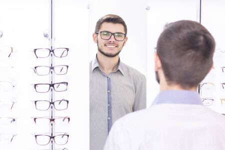 healthcare, people, vision and vision concept. men smiling trying on glasses in the store.の写真素材