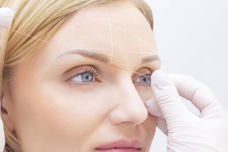 girl beautician marks with the help of thread eyebrow tattoo. Permanent makeup. Permanent tattooing...