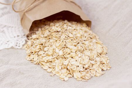 dry natural oat flakes. Oatmeal from an ecological paper bag. Natural linen background with eco bag...