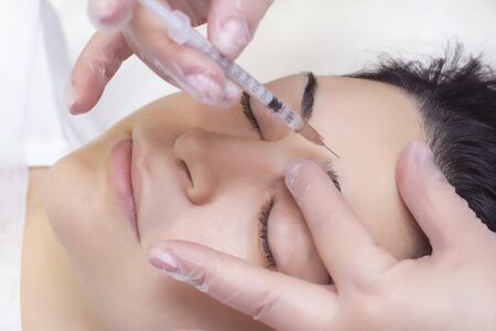 Close-up of a beautician injecting into forehead wrinkles. She holds a syringe. Cosmetics injected womans faceの写真素材