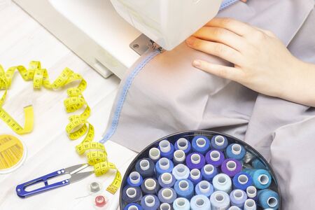 Background sewing. Hands of a seamstress on a sewing machine. Sewing studio concept. Threads,...