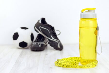 ball and cleats, measuring tape and a water bottle for writing on a light wooden background. preparation for the summer season and the beach, weight loss and sports conceptの写真素材