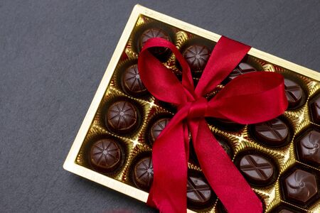 chocolate candies in a box with a red bow on a black background. dark photo, mood.の写真素材